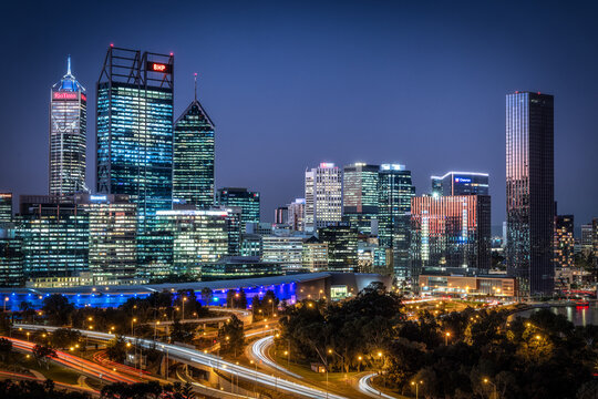 Perth, Australia - 16 May 2025: View of the city's skyline ablaze with light, a symphony of glass and steel reflecting the twilight sky, while below, ribbons of light trace the paths of winding roads.