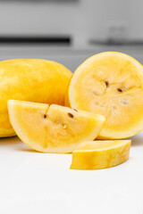 Yellow watermelon slice on reflective white surface with whole fruit in background