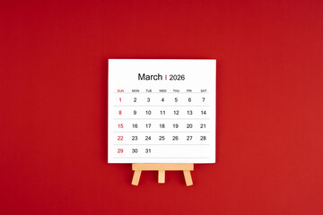 Calendar page for March 2026 with wood easel on a dark red background.