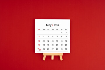 Calendar page for May 2026 with wood easel on a dark red background.