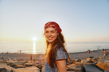 lifestyle woman in modern boho-western denim street style smiles warmly on rocky beach at sunset...