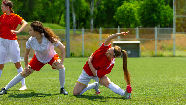 Female football players get ready under the sun on a grassy field. Concept of body positivity through movement, dynamic team warm-up, physical awareness and motivation.