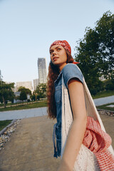 lifestyle woman in modern boho-western denim street style wears red bandana and carries knit bag in...
