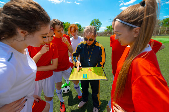 Female soccer team planning strategy with coach on sunny day at outdoor field. Concept of tactical learning and sports education, teamwork and competitive preparation.