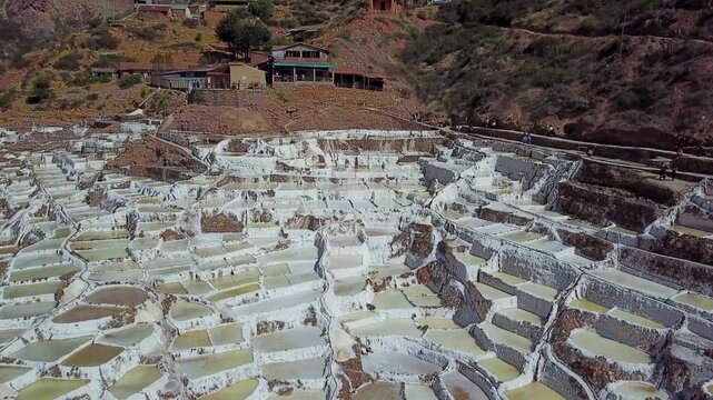 Aerial view of the terraced Maras Salt Mines creating a mesmerizing patchwork of white and earthen tones against the rugged landscape, Urubamba, Cusco, Peru.