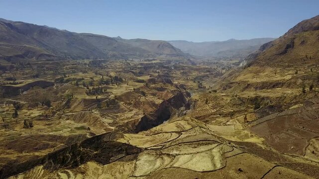 Aerial view of the Colca Canyon, a rugged landscape with terraced farming and steep cliffs, showcasing the canyon's vastness and the textures of the terrain, Chivay, Arequipa, Peru.