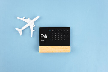 February 2026 black wooden calendar and airplane toy on blue color background.