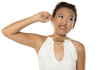 Young Kazakh woman scratching her ear with discomfort, studio shot on white background.