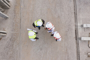 Aerial top-down view of diverse engineers and supervisors forming a circle during planning discussion at concrete prefab factory, showing unity and teamwork culture.