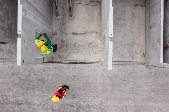 Aerial view of multicultural engineering team inspecting layout at precast concrete panel factory, surrounded by large structural wall elements in organized production yard.