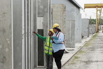 Southeast Asian female site inspector evaluates vertical precast concrete panels with field worker...