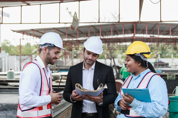 Team of engineers reviewing construction documents and plans on site. Surrounded by concrete panels and heavy machinery, they demonstrate teamwork and coordination in a real industrial setting.