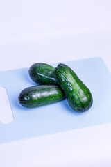 Three dark green zucchinis lie on a light blue cutting board. The zucchinis are shiny and fresh, stacked one on top of the other. Cooking, emphasizing the freshness and texture of the zucchinis.