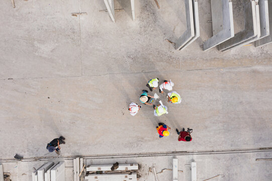 Aerial top-down view of diverse engineers and supervisors forming a circle during planning discussion at concrete prefab factory, showing unity and teamwork culture. - Powered by Adobe