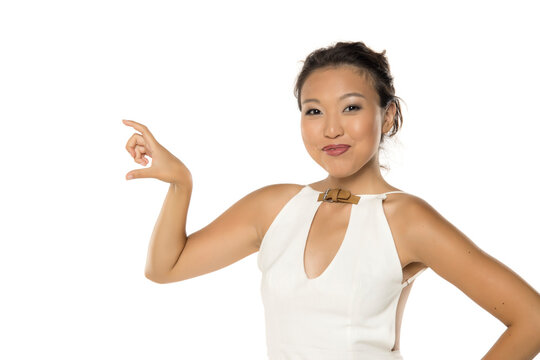 Smiling Asian woman holding invisible small product with fingers, studio shot on white background.