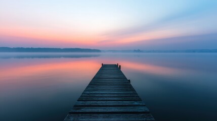 Obraz premium A wooden pier leads into a tranquil lake at dusk. The water perfectly reflects the soft pastel colors of the sunset sky, creating a serene and minimalist landscape