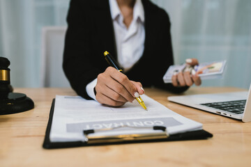 A lawyer in formal attire holds money and balances scales of justice, symbolizing legal decisions, fairness, and ethics, with a gavel, contract, and documents on the desk.