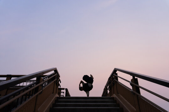 夕暮れの歩道橋で片手倒立を決めるブレイクダンサーのシルエット