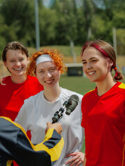 Smiling female football players interviewed after game on sunny day. Concept of representation in media, diversity and sport coverage campaigns.