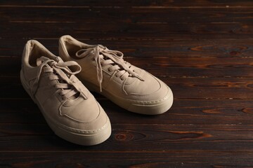 Pair of beige sneakers on wooden surface, space for text