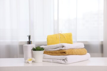Stack of colorful towels, liquid soap and floral decor on white table indoors,
