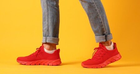 Man wearing pair of red sneakers on yellow background, closeup