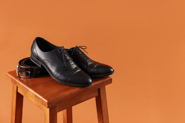 Pair of black leather shoes on stool against brown background. Space for text