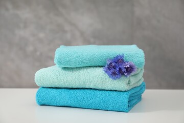 Stack of colorful towels and flowers on white table, closeup