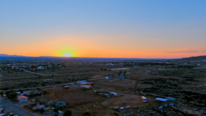 Aerial view of the Grants New Mexico landscape during sunset with a sprawling, semi-arid terrain. Sparse infrastructure includes low-lying buildings, roads, and some vegetation.