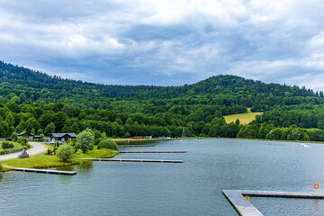 Peaceful lake surrounded by lush green hills with wooden piers and forest in the background.