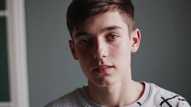 Young male exhibiting nuanced emotional states while standing in minimalist indoor space, conveying introspective mood through subtle facial expressions and quiet demeanor