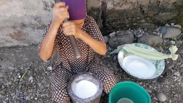 A woman manually pounds rice using a mortar or pestle, a traditional tool for grinding rice into flour. This traditional method is still used in Aceh Province.