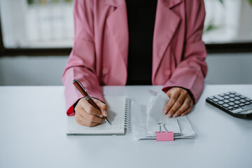 A woman holding receipt and using a calculator, sitting at a table indoors, calculating her expenses