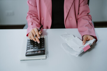 Happy woman managing her finances at home, using a smartphone to check her expenses while holding a...