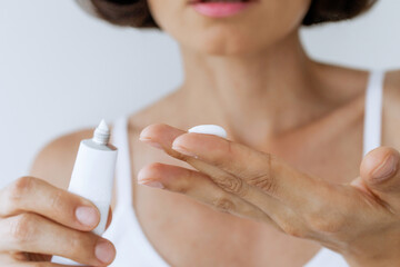 Woman Applying ointment  from White Tube on Finger – Skincare, Treatment, Dermatology, Close-Up of Hands with Soft Focus Face in Background