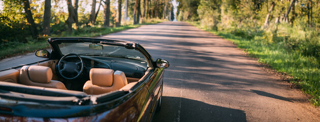 An open-top convertible stands in an alley on a sunny summer day. There are no people, no one. The body and interior of a car without a roof.