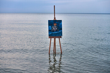 Easel with striking abstract painting stands in calm ocean waters, creating surreal ambiance. Scene...