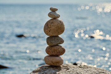 Stack of smooth stones precariously balanced on larger rock by calm seaside, symbolizes balance and serenity, evoking peaceful and meditative atmosphere