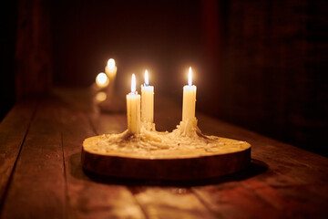 Four lit candles on wooden base illuminate rustic table in dark, cozy and peaceful atmosphere....