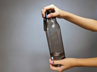 Close-up of a person holding a transparent gray water bottle partially filled with clear liquid...