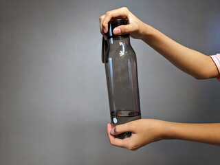 Close-up of a person's hands holding a translucent dark grey reusable water bottle filled with...