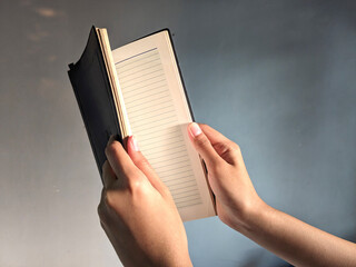 Close-up of a person's hands holding open a lined notebook against a softly lit grey background,...