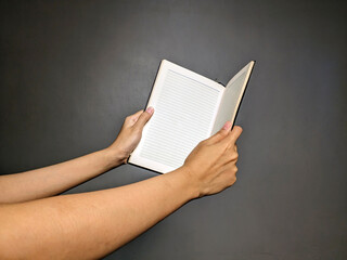 Close-up of a person's hands holding open a lined notebook against a dark, plain background,...