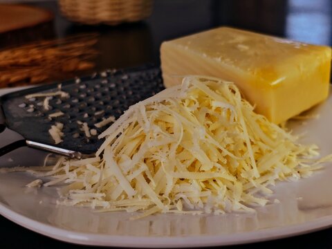 Freshly Grated Cheese with Block and Grater on White Plate, Culinary Preparation