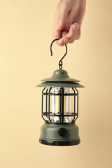 Hand holding lantern lamp on beige background. Camping