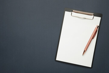 Black tablet with piece of empty paper and pen on dark blue background. Space for text
