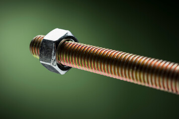 Close-up of large steel screw with bolt on green background.