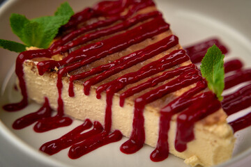 Delicious cheesecake topped with rich berry sauce and fresh mint leaves, a perfect dessert to satisfy any sweet tooth craving and elevate your dining experience.