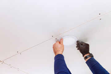 Skilled electrician is installing circular ceiling light fixture in modern home interior.