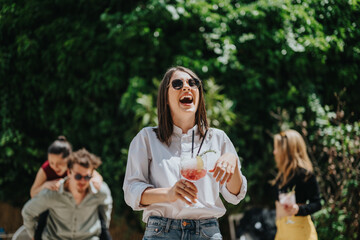 A cheerful group of young adults spending quality time outdoors while drinking cocktails and having...